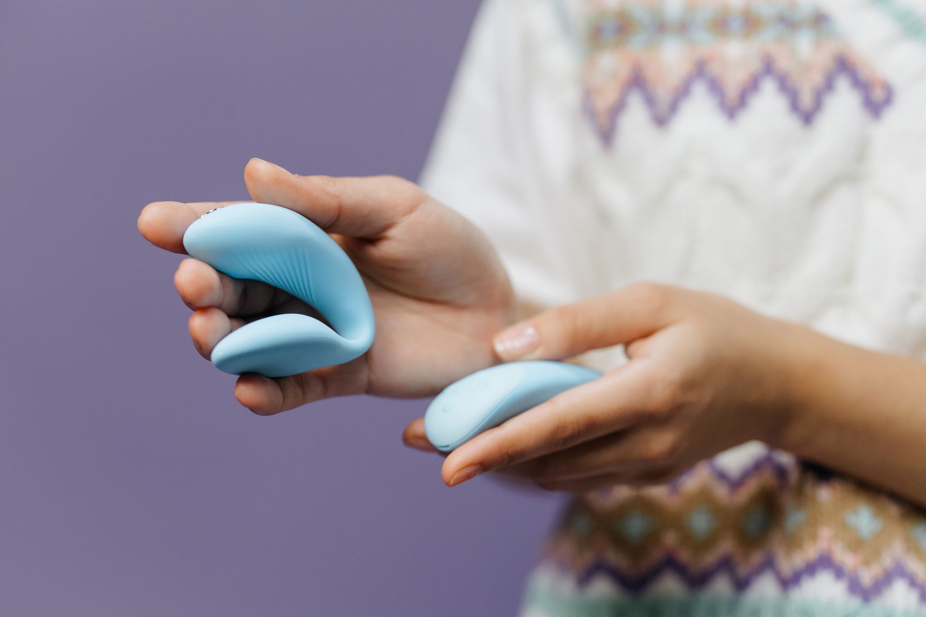 Close-up of hands holding a sleek blue clitoral vibrator against a purple background, symbolizing modern pleasure exploration.