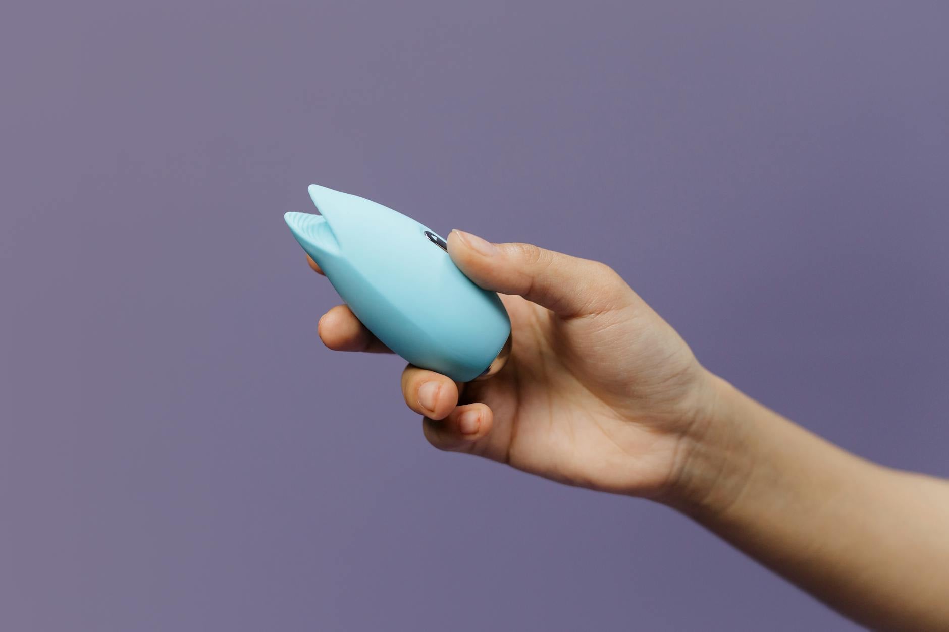 A blue lemon clitoral vibrator held in hand against a purple background, representing modern intimacy tools